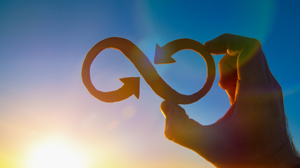 A symbol of infinity in the hand of a man against the sky and the glare of the sun, business...