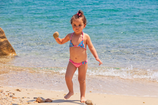 A little cute baby girl is playing on a beach near a sea on holiday