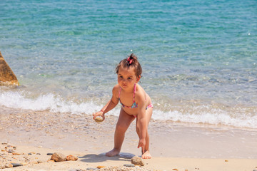 A little cute baby girl is playing on a beach near a sea on holiday