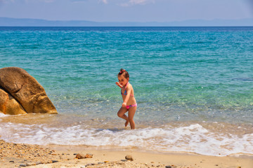 Fototapeta na wymiar Cute little girl running at the beach near the sea on vacations.