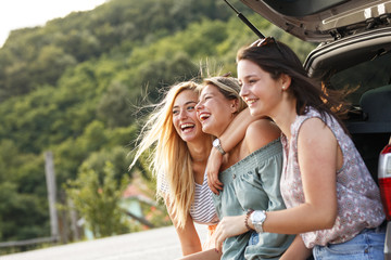 Group of female best friends on travel. They're sitting on a car trunk and relaxing after a long journey.  © BalanceFormCreative