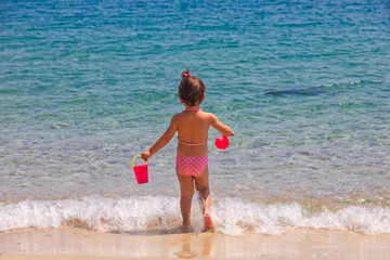 Rear view of a little cute girl is playing on a beach near the sea on vacations.