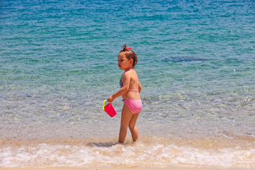 A little cute baby girl is playing on a beach near the sea on holiday