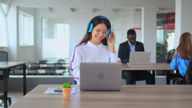 Pretty young lady has headphones on her head. She is chilling and moving intempoof music. Then she looks straight into camera and smiles