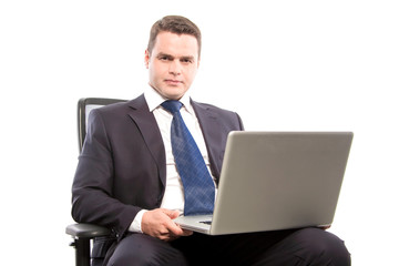 Serious businessman holding a laptop in his hands while sitting in a chair.