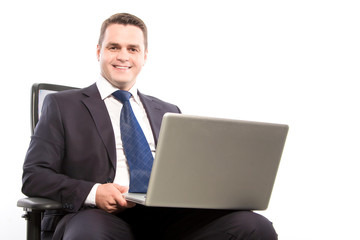 A smiling businessman holds a laptop while sitting in a chair. Close-up.