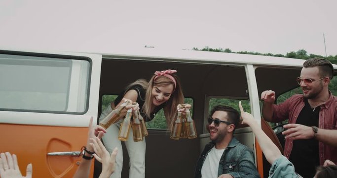 Starting the picnic party young lady taking lots of bottles of beer from the retro van and giving them to her friends and happy starting drinking. 4k