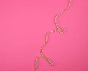 twisted golden cable in a textile winding on a pink background
