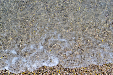 Sea foamy wave on a pebble beach top view