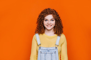 Curly- haired funny woman smiling and looking at camera on orange background