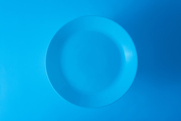 An overhead view of empty blue plate against blue background