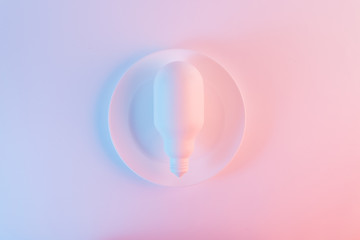 White light bulb on plate against blue and pink background
