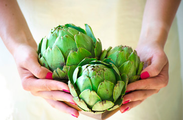 Hands of young white woman holding brown wooden bowl. Artichokes close up. Artichoke flowers in rustic bowl. Healthy eating concept, vegetable background, natural eco products. Selective focus image.