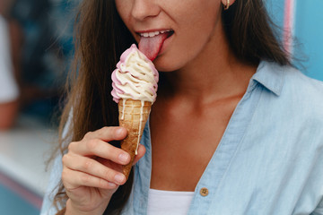 Young woman eating sweet ice cream cone in summer hot weather in street