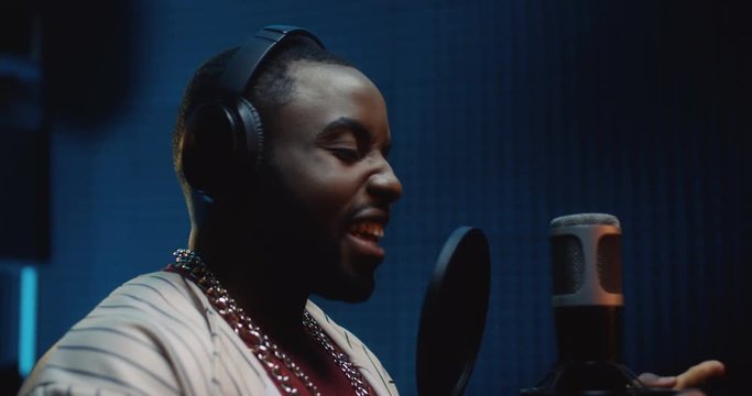African American attractive smiled and stylish r'n'b or blues male singer recording a vocal in the sound studio while singing in the microphone. Close up.