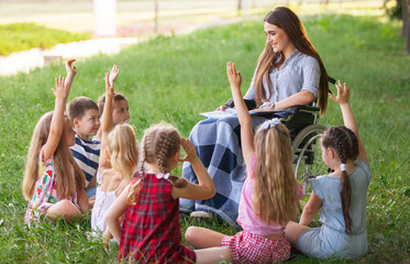 children hold a lesson with the teacher in the park on a green lawn.