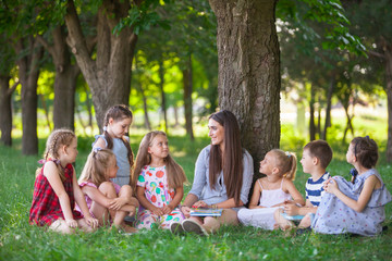 children hold a lesson with the teacher in the park on a green lawn.