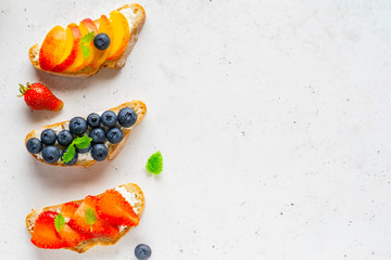 Various toasted bread with peach, blueberry, strawberry, ricotta (cream cheese), mint.
