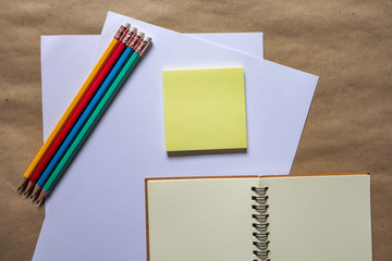 Multi-colored pencils and brown notebooks on a white background can be used to make backgrounds. Education, yellow note paper, education