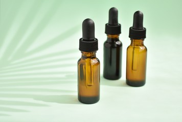 Aromatherapy, dropper bottles with essential oils on green background with palm leave shadow,...
