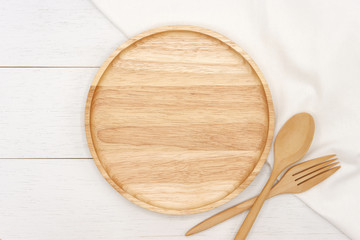 Empty round wooden plate with spoon, fork and white tablecloth on white wooden table. Top view image.