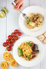 seafood risotto and fettuccine pasta at white wooden table top. woman hand with fork is takes some of rice. Italian cuisine concept with free space for your text. Copy space