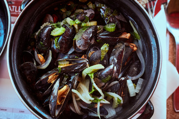 Top view of fresh paleo mussels in marine style - Moules mariniere - served hot in traditional french dark pot with green vegetables