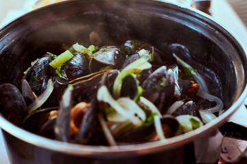 Fresh paleo mussels in marine style - Moules mariniere - served hot in traditional french dark pot with green vegetables