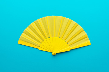 Top view of opened yellow fan mockup over blue turquoise background. Minimalist flat lay photo of folding fan with central composition.