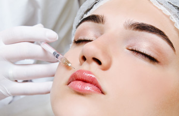 The doctor cosmetologist beautician makes the rejuvenating facial botox injections procedure for tightening and smoothing wrinkles on the face skin to lips of a beautiful young woman in a beauty salon
