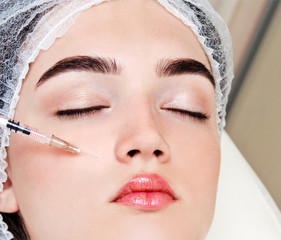 The doctor cosmetologist beautician makes the rejuvenating facial botox injections procedure for tightening and smoothing wrinkles on the face skin of a beautiful young woman in a beauty salon.