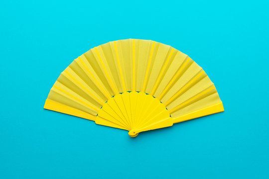 Top view of opened yellow fan mockup over blue turquoise background. Minimalist flat lay photo of folding fan with central composition.