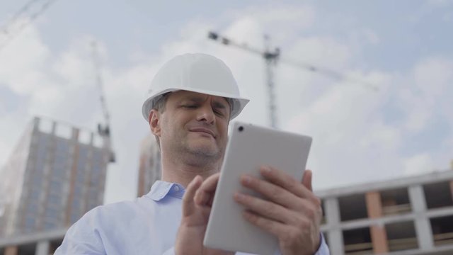 A man in a helmet works on his laptop at a construction site, close-up. 4K