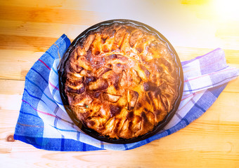 food, culinary and cooking concept - close up of apple pie in baking mold with kithchen towel on wooden table