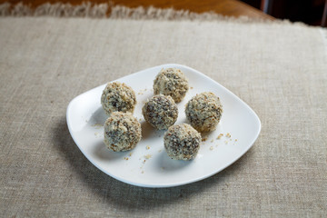 Homemade candy in the form of balls of dried fruit and walnut on a white plate on a linen napkin on the table. Healthy food without sugar and gluten.