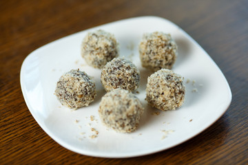 Homemade candy in the form of balls of dried fruit and walnut on a white plate on the table. Healthy food without sugar and gluten.