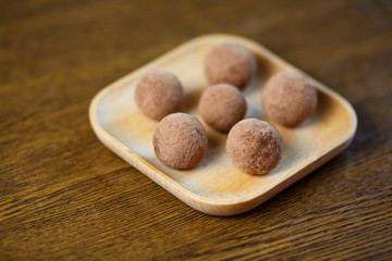 Homemade candy in the form of balls of dried fruit and cocoa powder on a wooden plate on the table. Healthy food without sugar and gluten.
