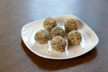 Homemade candy in the form of balls of dried fruit and walnut on a white plate on the table. Healthy food without sugar and gluten.