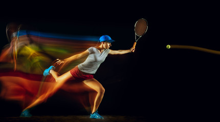 One caucasian woman playing tennis isolated on black background in mixed and stobe light. Fit young...
