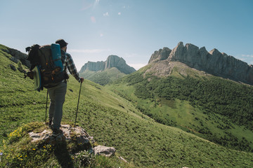  young guy with a tourist backpack looks at the mountain peaks on a sunny summer day