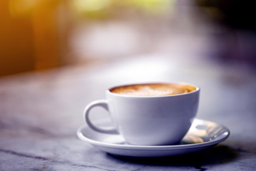 The  white ceramic cup of hot capuccino coffee on the wooden table in the restaurant or coffee shop with flare in the natural light , violet or blue light theme. 