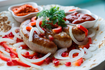 Fried pork sausages on pita bread with ketchup and Armenian appetizer Aivar with vegetables. Lavash, red bell pepper, onions, sausages. Oktoberfest food, the concept of the pub