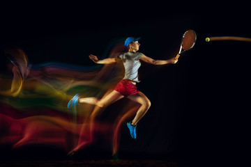 Fototapeta na wymiar One caucasian woman playing tennis isolated on black background in mixed and stobe light. Fit young female player in motion or action during sport game. Concept of movement, sport, healthy lifestyle.