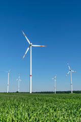Low angle view of five wind power turbines, part of a wind farm, on a green field in eastern Germany near the city of Cottbus, Brandenburg. Wind turbines are part of the energy transition strategy.