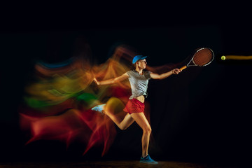 One caucasian woman playing tennis isolated on black background in mixed and stobe light. Fit young female player in motion or action during sport game. Concept of movement, sport, healthy lifestyle.