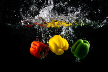 Three Paprika splash in water on black background, Capsicum annuum: bell pepper and buble.