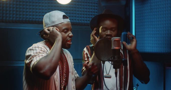 African American young male singers in a duo singing or reading a rap while recording a hit song in the sound studio.