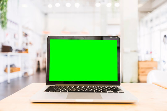 Mockup image of laptop with blank Green screen on wooden table of In the coffee shop.