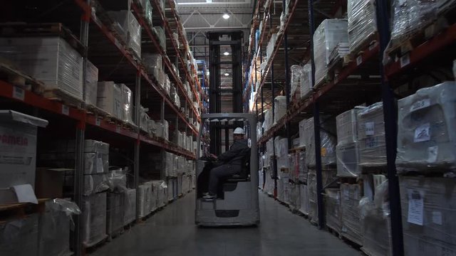 Forklift moves between racks with products. Logistics warehouse. 4K Slow Mo