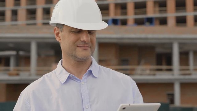 Millennial Hispanic architect on construction site wearing hard hat helmet. Latino job foreman contractor using tablet computer. 4k